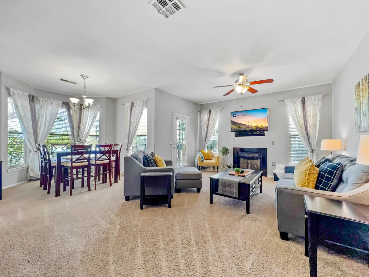 A cozy living and dining area features comfortable seating, a large dining table set for meals or games, a television for entertainment, and decorative artwork. The space invites socializing, movie nights, and shared meals.
