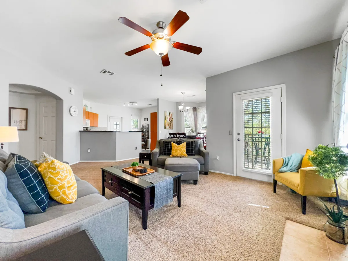 A bright, comfortable living area with a stylish yellow accent chair, decorative throw pillows, a coffee table, and a sliding door that opens to an outdoor space. Sunlight streams in, suggesting a seamless flow between indoor comfort and opportunities to step outside.