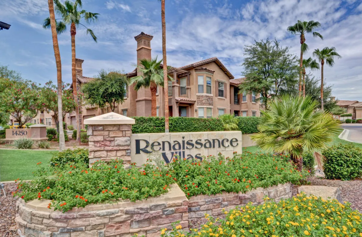A welcoming shot of the Renaissance Villas sign set within a beautifully landscaped garden, with surrounding palm trees and a glimpse of the charming exterior architecture. The scene embodies the serene, resort-style setting of the gated community and its lush communal spaces.