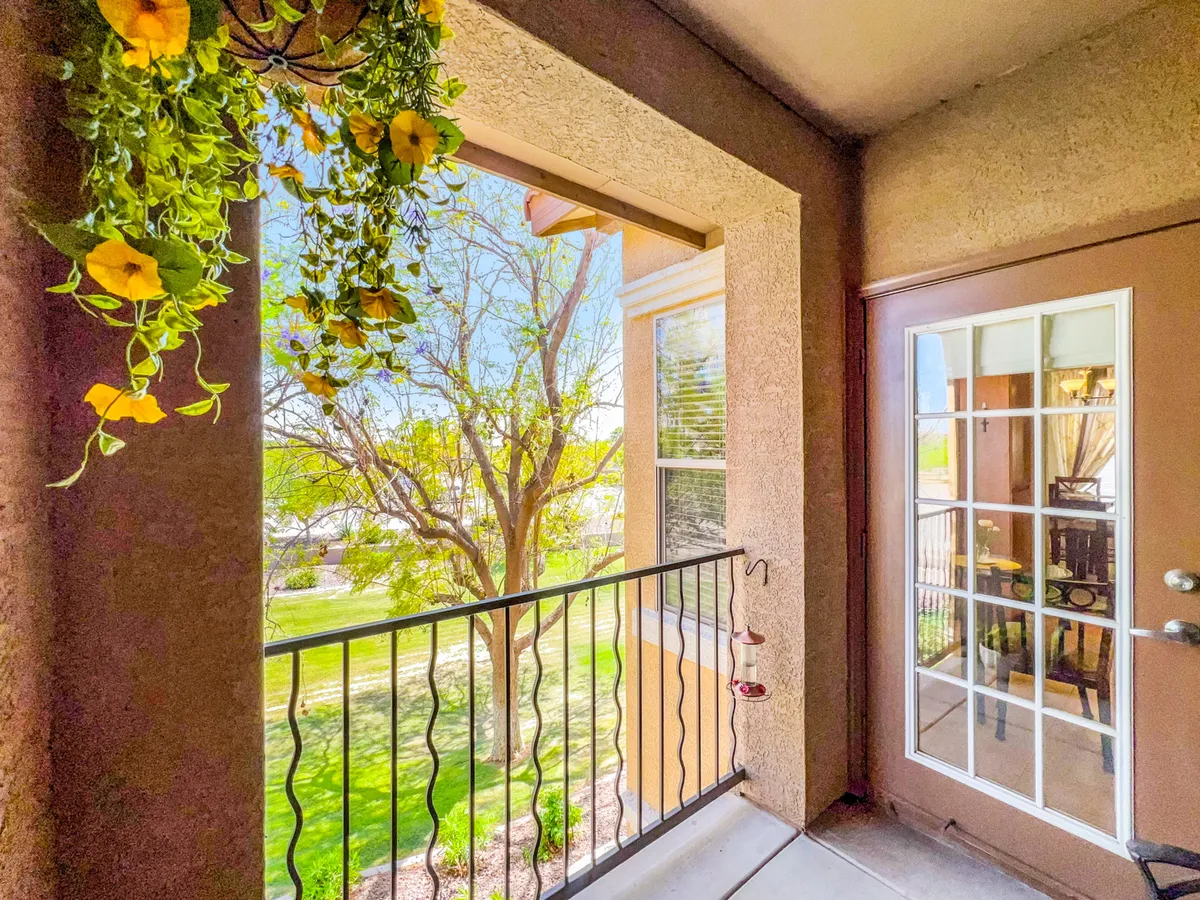 A charming exterior view with hanging flowers and a glass-paned door, offering a peek into a welcoming patio or balcony space. The mood is relaxed and inviting—suggestive of enjoying a morning coffee, reading, or unwinding while watching the sunset.