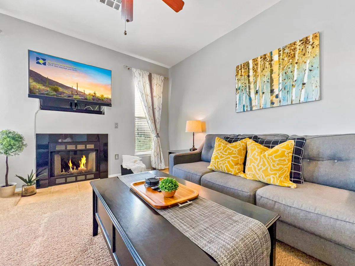 A spacious living room featuring a cozy sofa with yellow pillows, a modern fireplace, a television, and stylish artwork on the wall. The layout invites relaxation and socializing, with ample seating and a warm, inviting atmosphere.