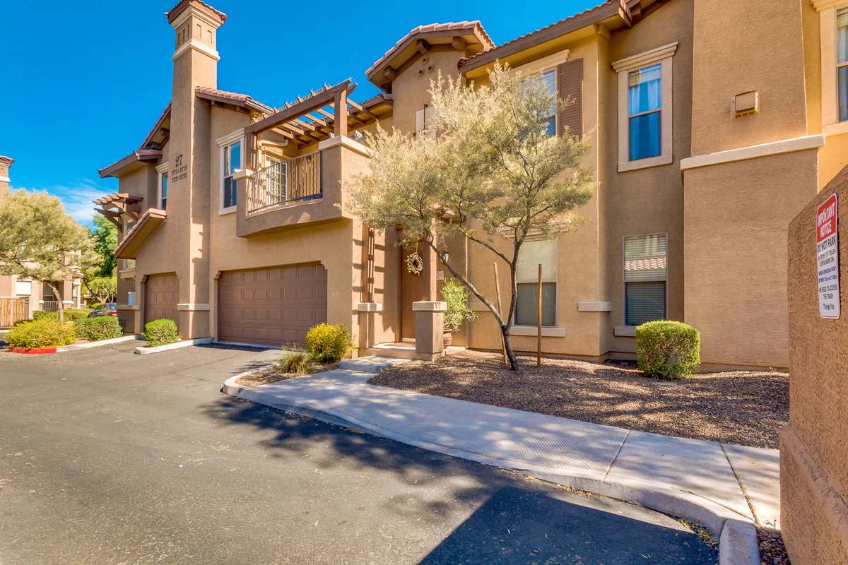 This exterior image showcases the architectural details of the condo building, a manicured front yard, and a paved pathway leading up to the entrance. The inviting design and visible balconies hint at opportunities to enjoy the outdoors and Arizona's pleasant climate.