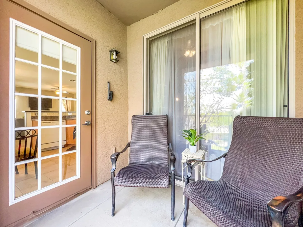 A cozy balcony setup with two chairs and a small table right at the doorway, inviting moments of relaxation or conversation. The scene captures the transition between indoor comfort and outdoor serenity.
