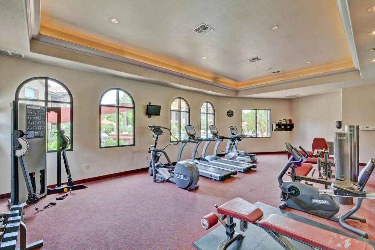 A modern fitness center filled with treadmills, elliptical machines, a weight bench, and large windows that allow natural light to pour in. The mood is active and motivating, perfect for daily workouts or group fitness sessions.